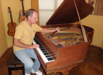Tim Rainwater works on tuning a baby grand piano in a home music room.